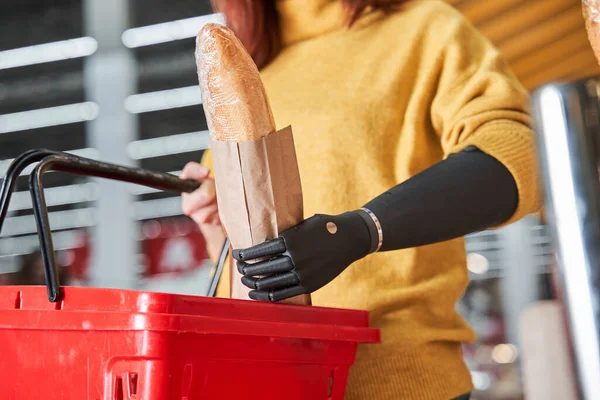 Mujer con extremidades artificiales poniendo criado en la cesta de alimentos —  Fotos de Stock