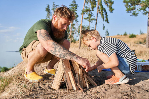Красивый папа и молодая дочь разожгли огонь в ожидании пикника.