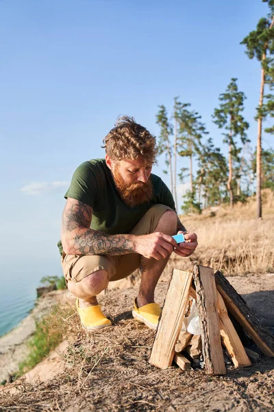 Concentrated man making fire while camping in wild forest — Stock Photo, Image