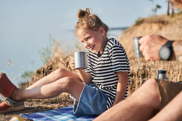 Chica calentando sus manos en una taza con té caliente mientras su padre sostiene su taza cerca — Foto de Stock