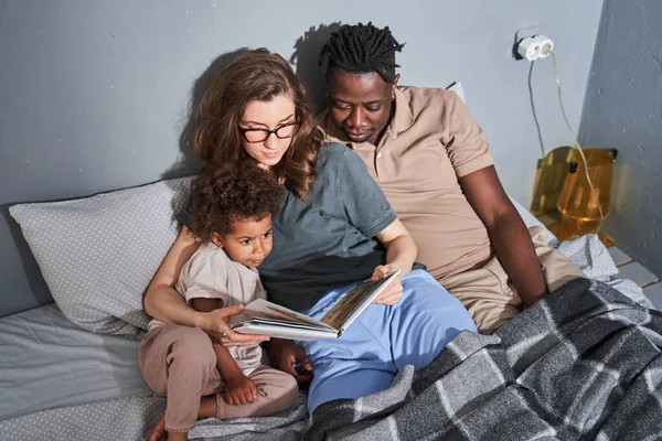 Маленькая девочка и ее родители участвуют в чтении удивительной книги — стоковое фото
