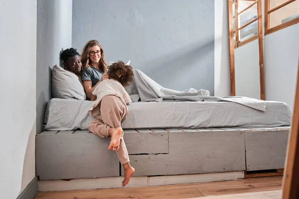 Meisje krijgen op het bed naar haar ouders terwijl het doorbrengen van luie ochtend samen — Stockfoto