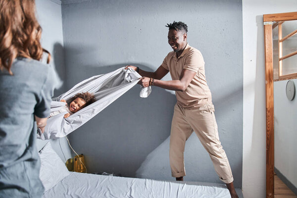 Девушка лежала у одеяла и громко смеялась, пока ее родители размахивали ею