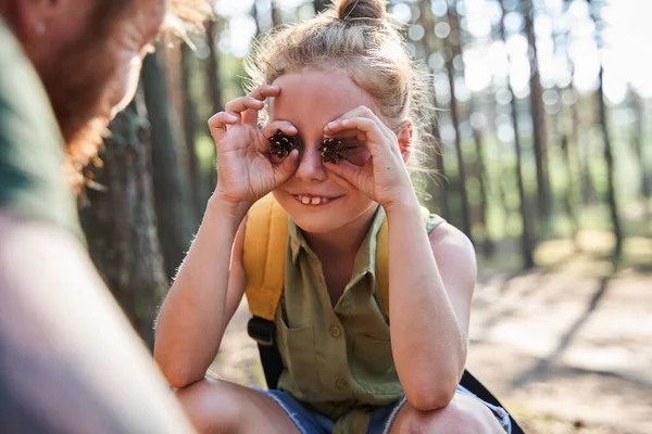 Dívka show borovice kužely na očích k otci v lese — Stock fotografie