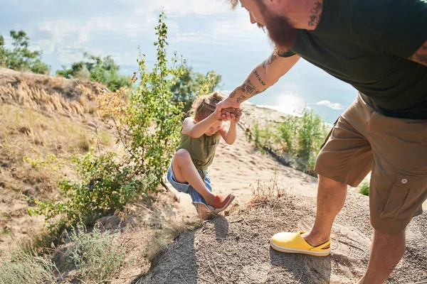 Mannen hjälper dottern att klättra på kullen vid kusten — Stockfoto