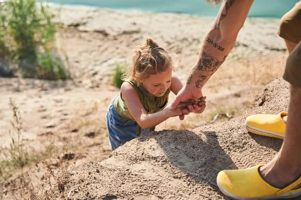 Muž pomáhá dceři při lezení na kopec na pobřeží — Stock fotografie