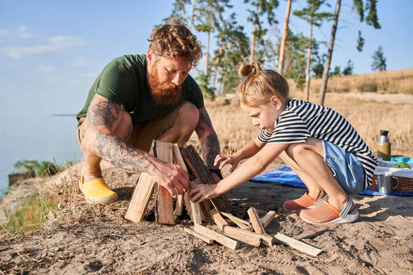 Vader en dochter maken vuur van boomstammen aan de kust — Stockfoto