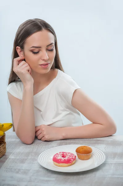 Hermosa chica joven está eligiendo entre frutas y comida dulce — Foto de Stock