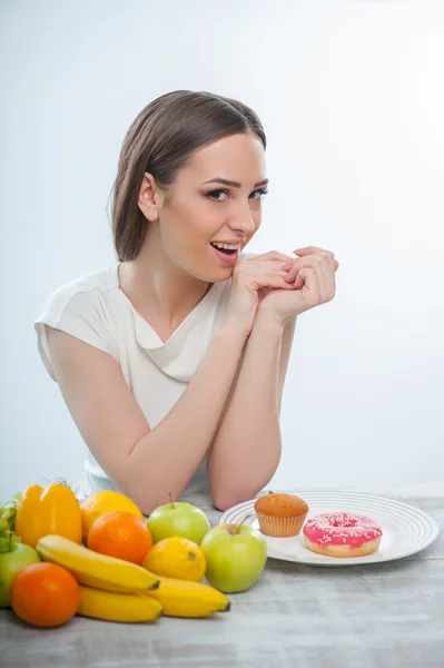 Cheerful young woman is choosing between healthy and unhealthy food — Stock Photo, Image