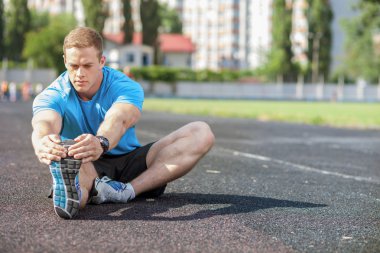Attractive young sportsman is doing warming-up in stadium