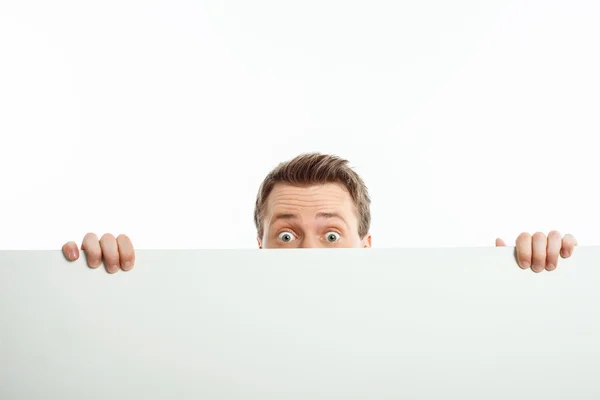 Attractive young man is hiding behind white wall Stock Picture