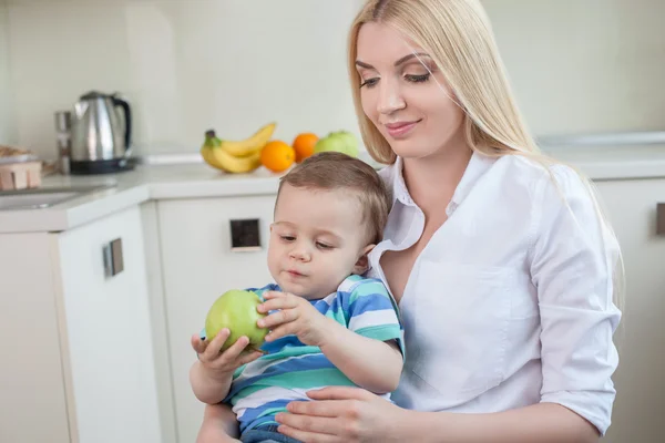 Csinos, fiatal Anya gyermekével, konyhában ül — Stock Fotó