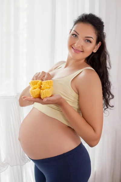 Beautiful young pregnant woman is playing with childlike booties — 스톡 사진