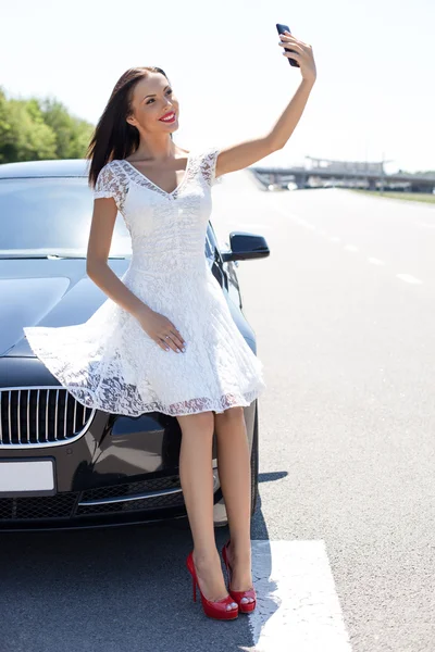 Attractive young woman is photographing herself near her car — Stock fotografie