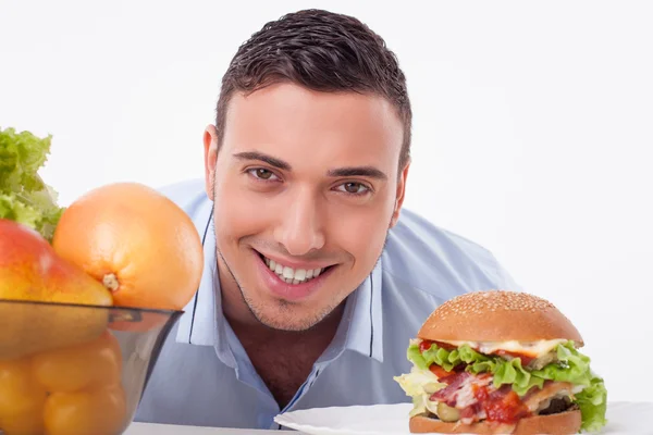 Handsome guy chooses between healthy and unhealthy food — Stock Photo, Image