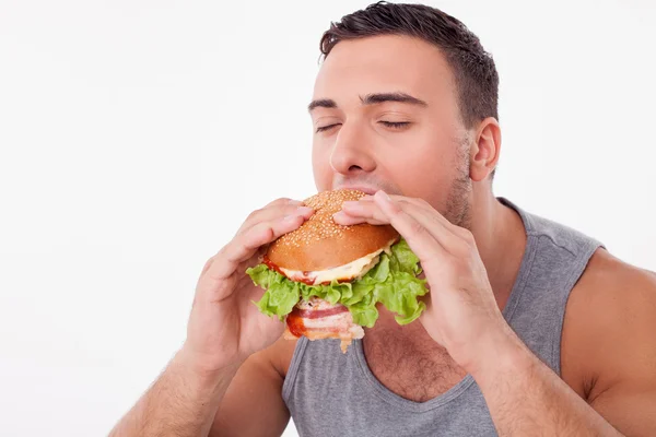 Attraente giovane uomo sta mangiando hamburger malsano — Foto Stock