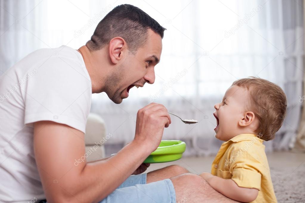 Handsome young man is feeding his child Stock Photo by ©iakovenko123