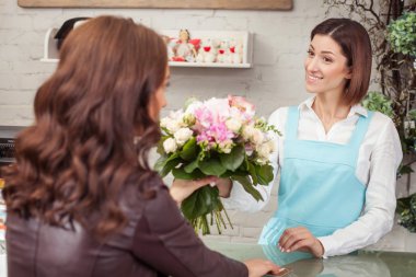 Cheerful young florist is selling a bouquet in store