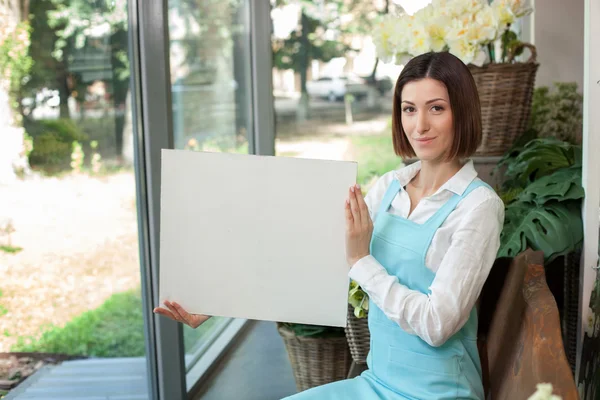 Attractive young saleswoman is showing billboard of flower shop — Stock Photo, Image