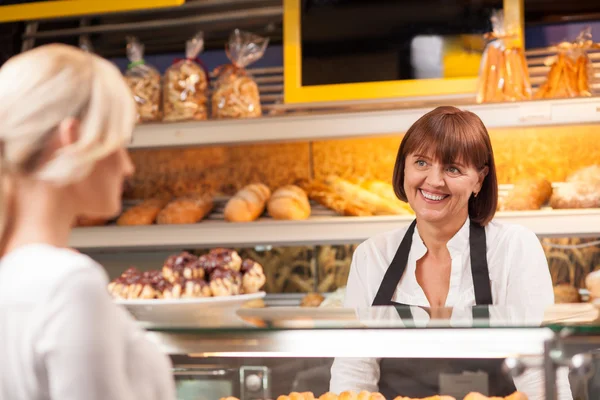 Весела продавщиця обслуговує клієнта в хлібопекарні — стокове фото