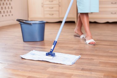 Skilled young housewife is cleaning floor with a mop