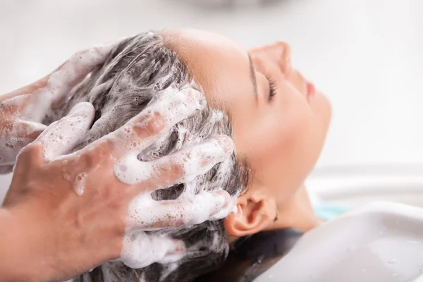 Cheerful young woman has her hair washed in beauty shop — Stock Photo, Image