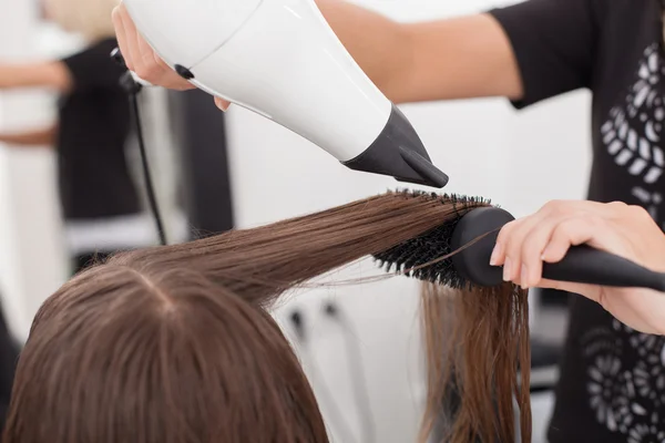 Cabeleireiro jovem experiente está usando um secador de cabelo no salão de beleza — Fotografia de Stock