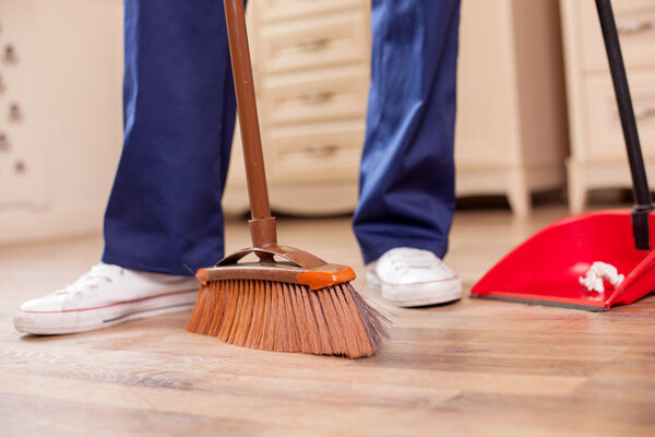 Skilled young male cleaner is cleaning floor in room