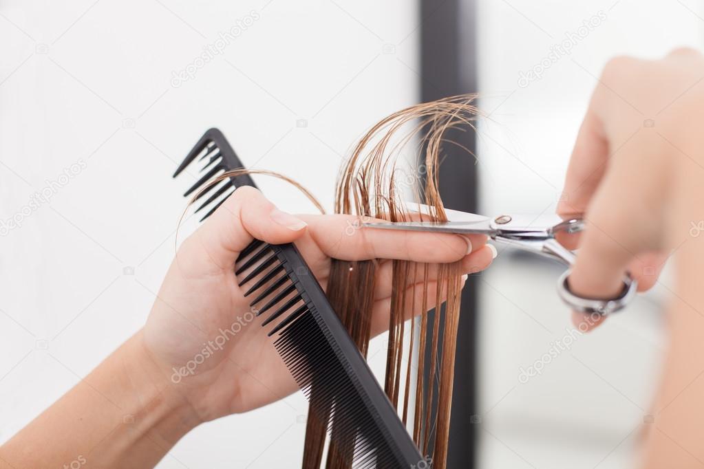 Skilled young hairstylist is making a haircut to her customer