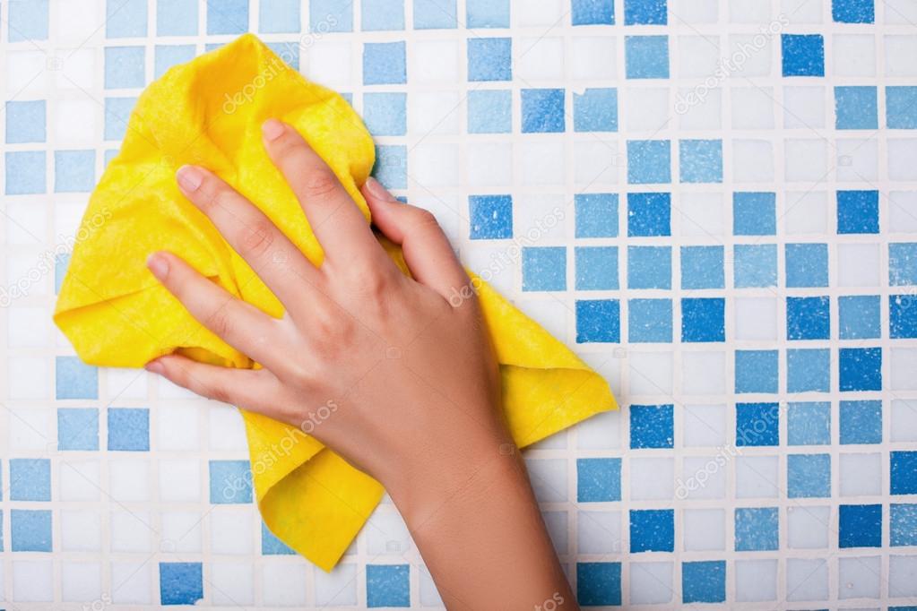 Cheerful maid is cleaning tiled surface with a wisp