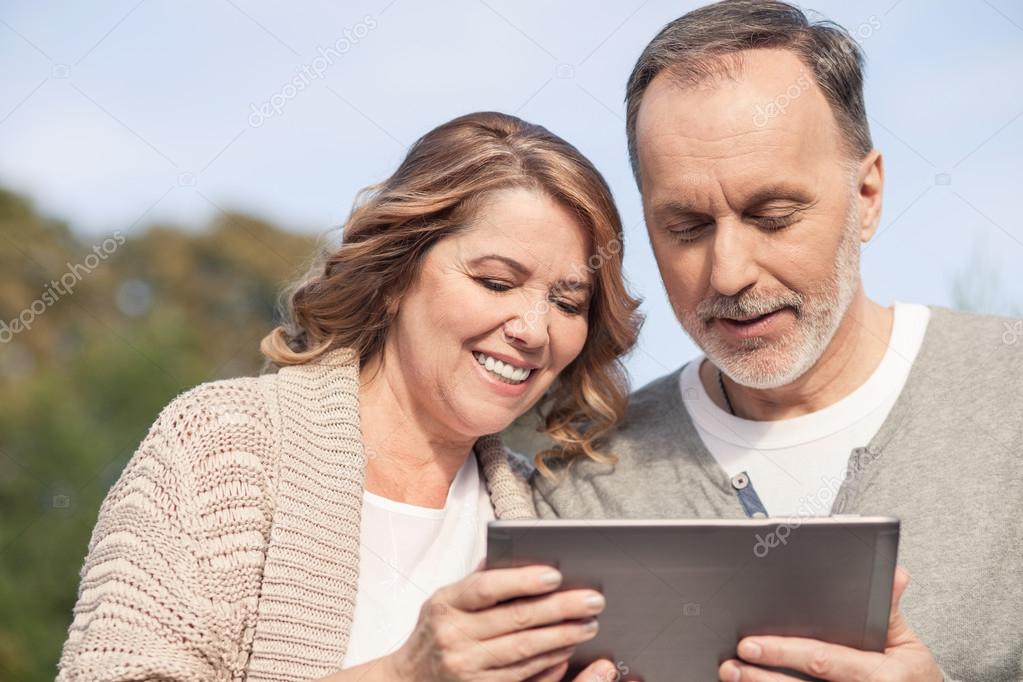 Cheerful old married couple is watching a tablet