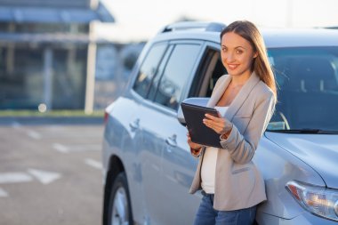 Cheerful young girl is holding laptop near vehicle