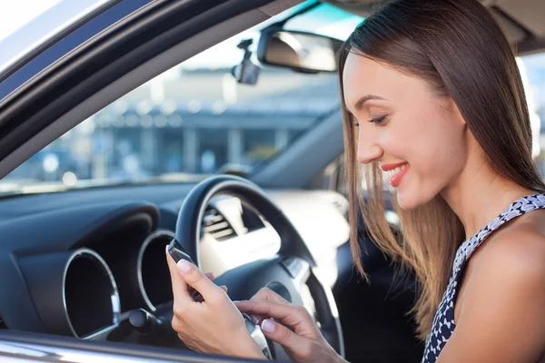 Giovane donna allegra sta usando il telefono in auto — Foto Stock
