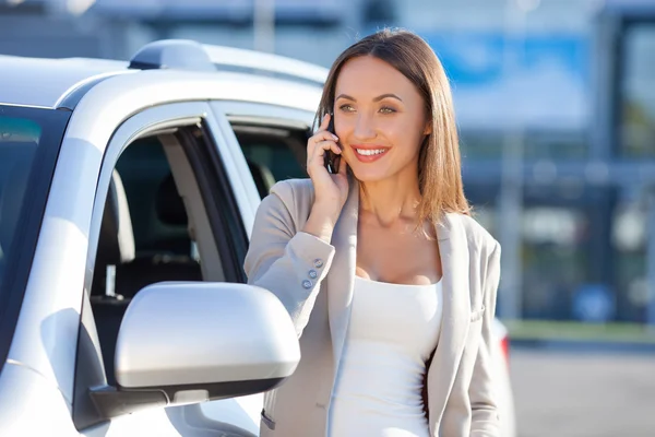 Attractive young woman is using telephone near vehicle — Stock Photo, Image