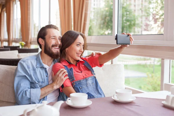 Alegre joven hombre y mujer están haciendo selfie en la cafetería — Foto de Stock