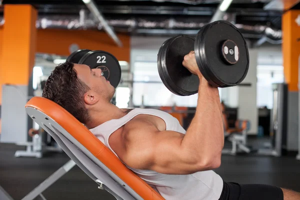 Attractive young male sportsman is training in gym — Stock Photo, Image