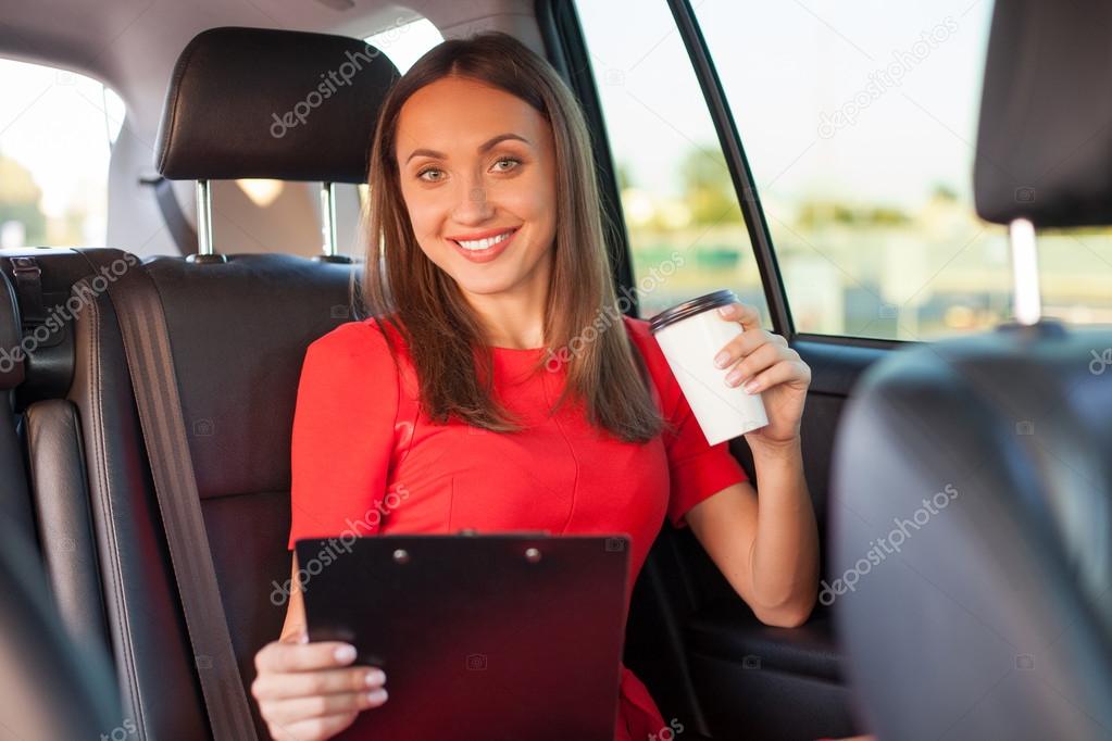 Cheerful young woman is enjoying hot drink in car