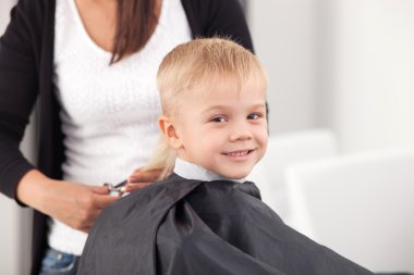Cheerful small child is getting haircut in hairdressing salon