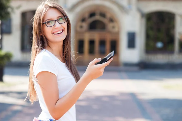 Cheerful young female student is using telephone outdoors — Stock Photo, Image