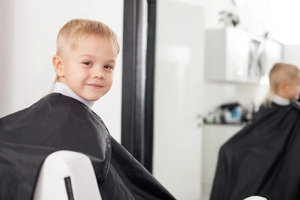 Cheerful male child is getting a hairstyle in hairdressers — Stock fotografie