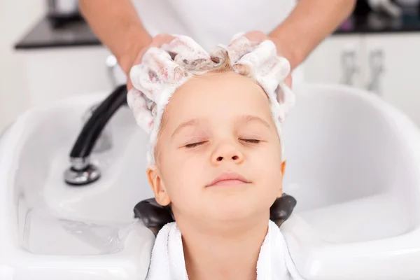 Skilled young hairdresser is treating hair of child — Stock fotografie