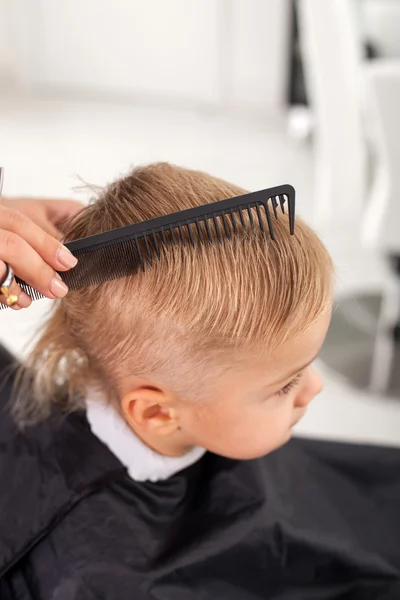 Professional young beautician is making hairstyle for child — Stockfoto