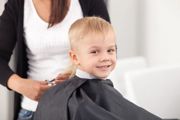 Criança pequena alegre está recebendo corte de cabelo no salão de cabeleireiro — Fotografia de Stock