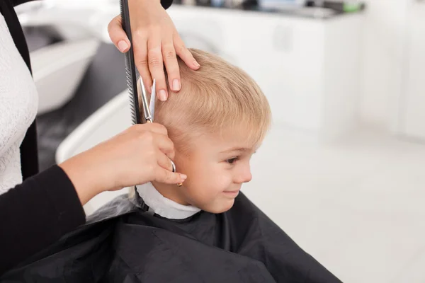 Skilled young female hairstylist is cutting human hair — Stockfoto