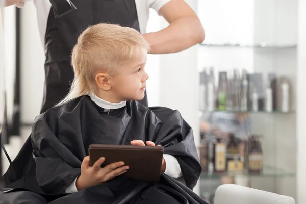 Professional young barber is making hairstyle for kid — Zdjęcie stockowe