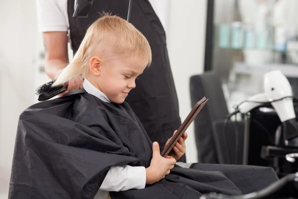 Professional young hairdresser is making hairstyle for child — Stockfoto