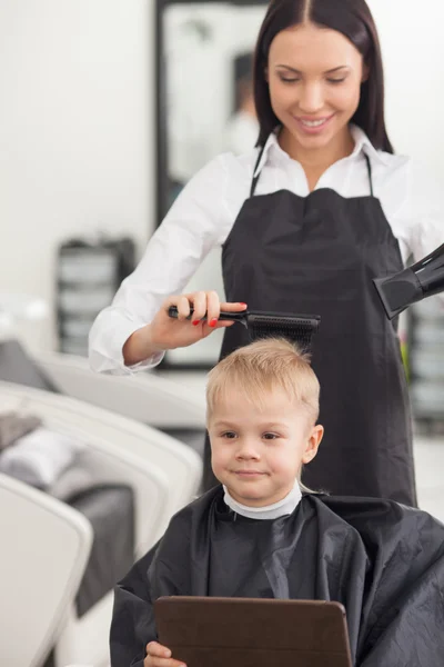 Cheerful young barber is using dryer in hairdressing salon — Stock Photo, Image