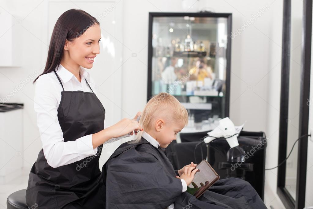 Attractive young female hairdresser is doing haircut