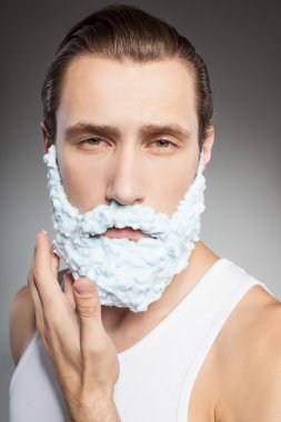 Attractive young bearded man shaves with joy