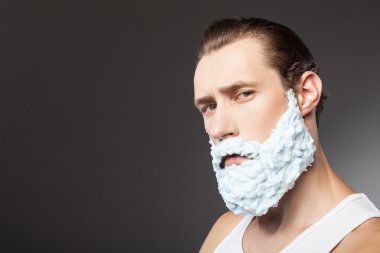 Cheerful young guy is shaving his beard